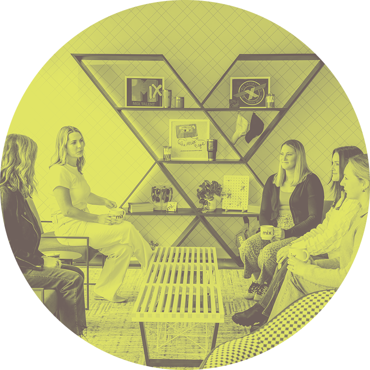 Group of women sitting in a modern office lounge having a discussion, with a large “X” shaped shelf and Mix branding in the background